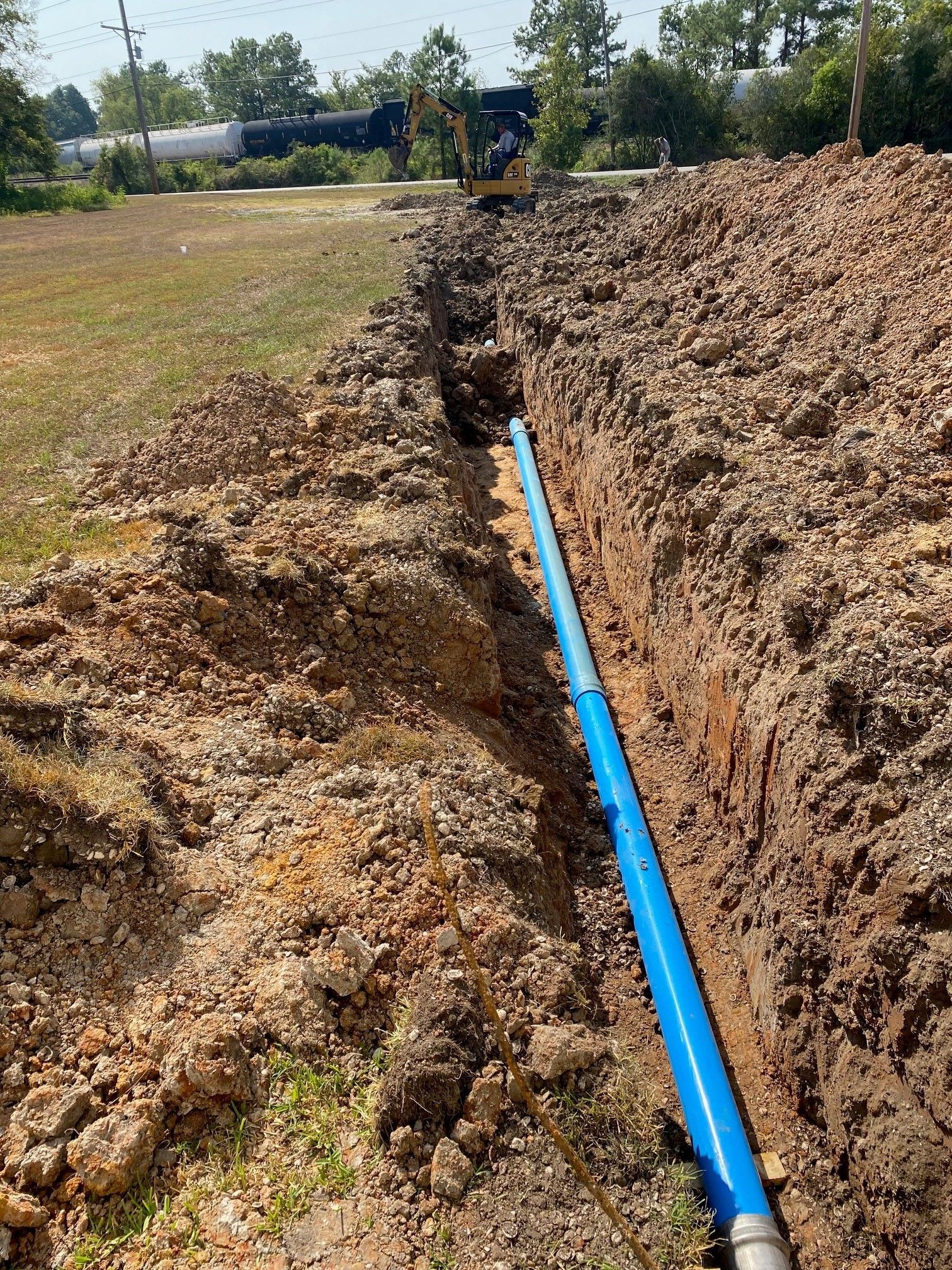 A blue pipe is being installed in a trench in the dirt.