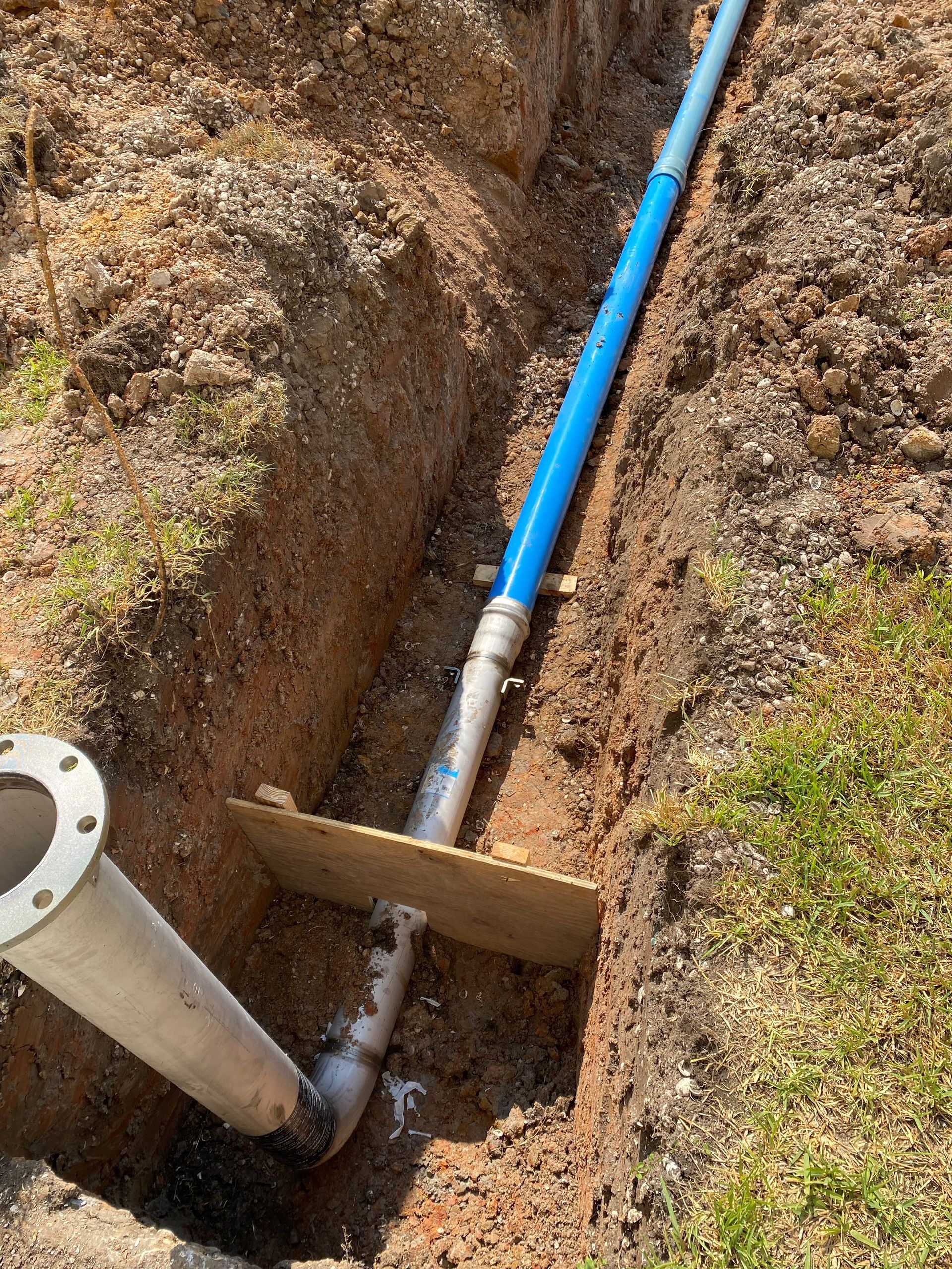 A blue pipe is laying in the dirt next to a metal pipe.