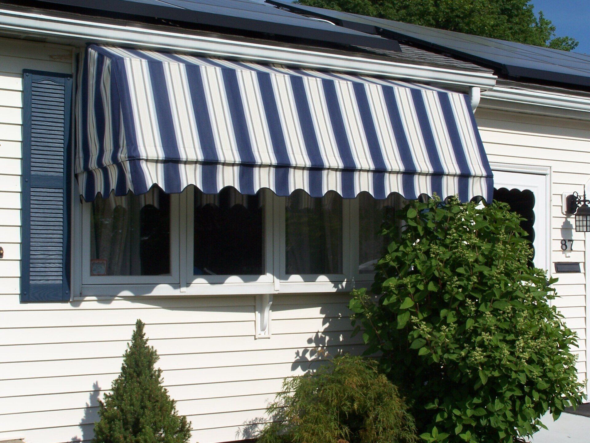 A white house with a blue and white striped awning over a window