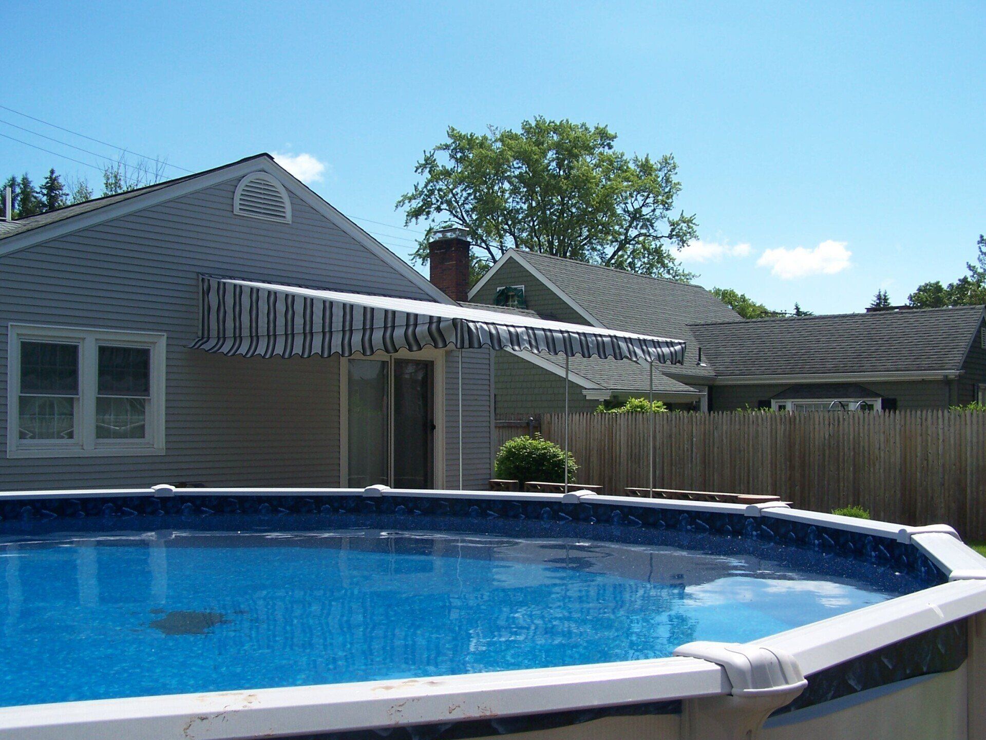A swimming pool in front of a house with an awning over it