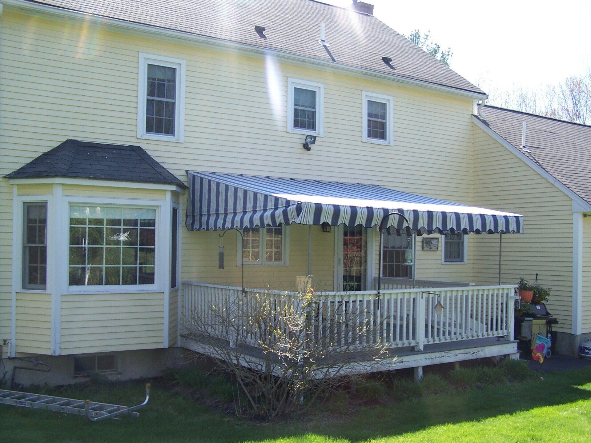 A yellow house with a blue and white awning on the porch