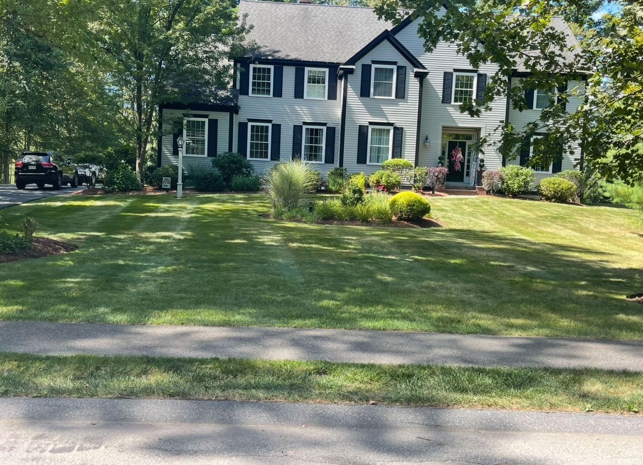 A large, two-story gray house with black shutters and trim sits behind a well-maintained lawn and mature trees.