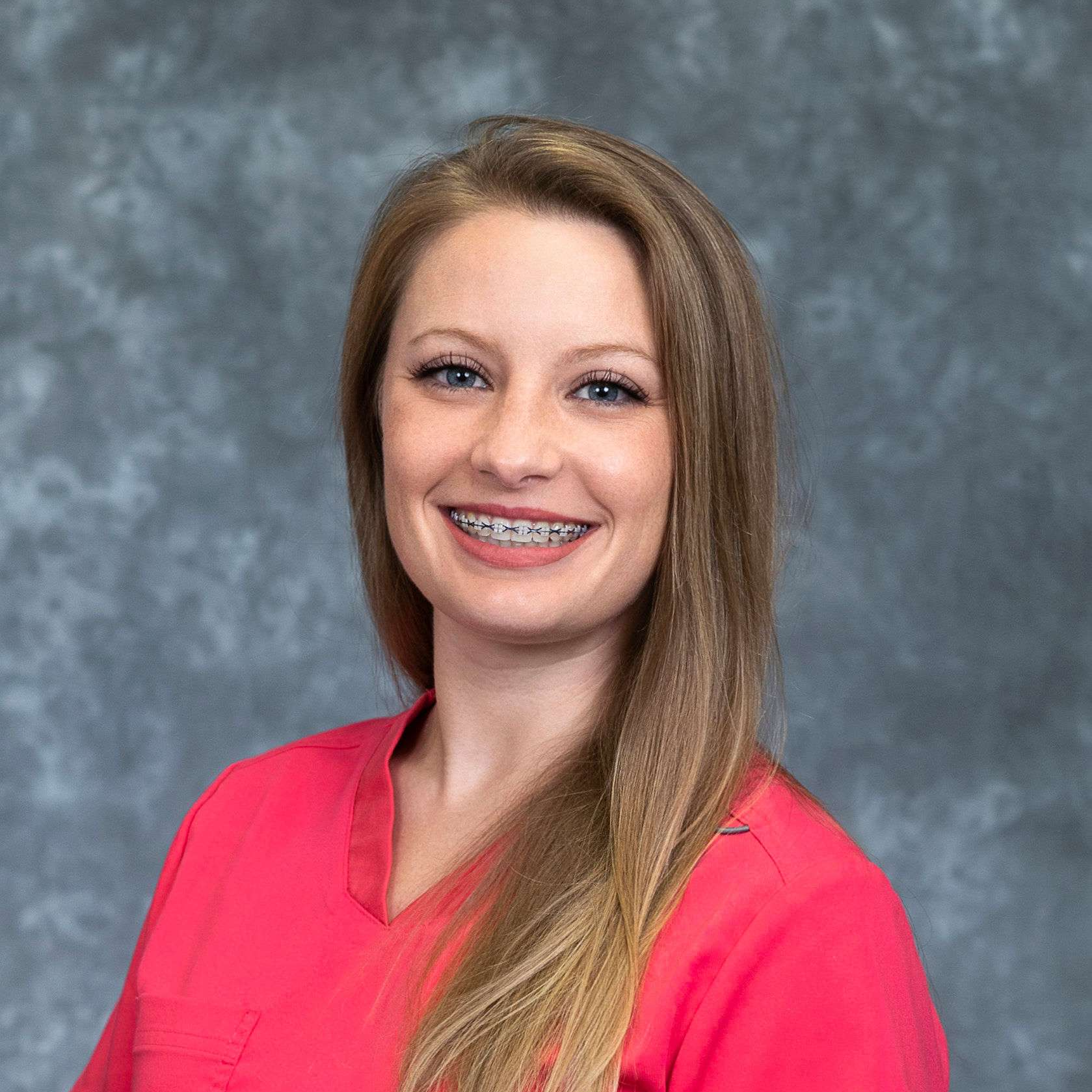 A woman wearing braces and a pink scrub top is smiling for the camera.
