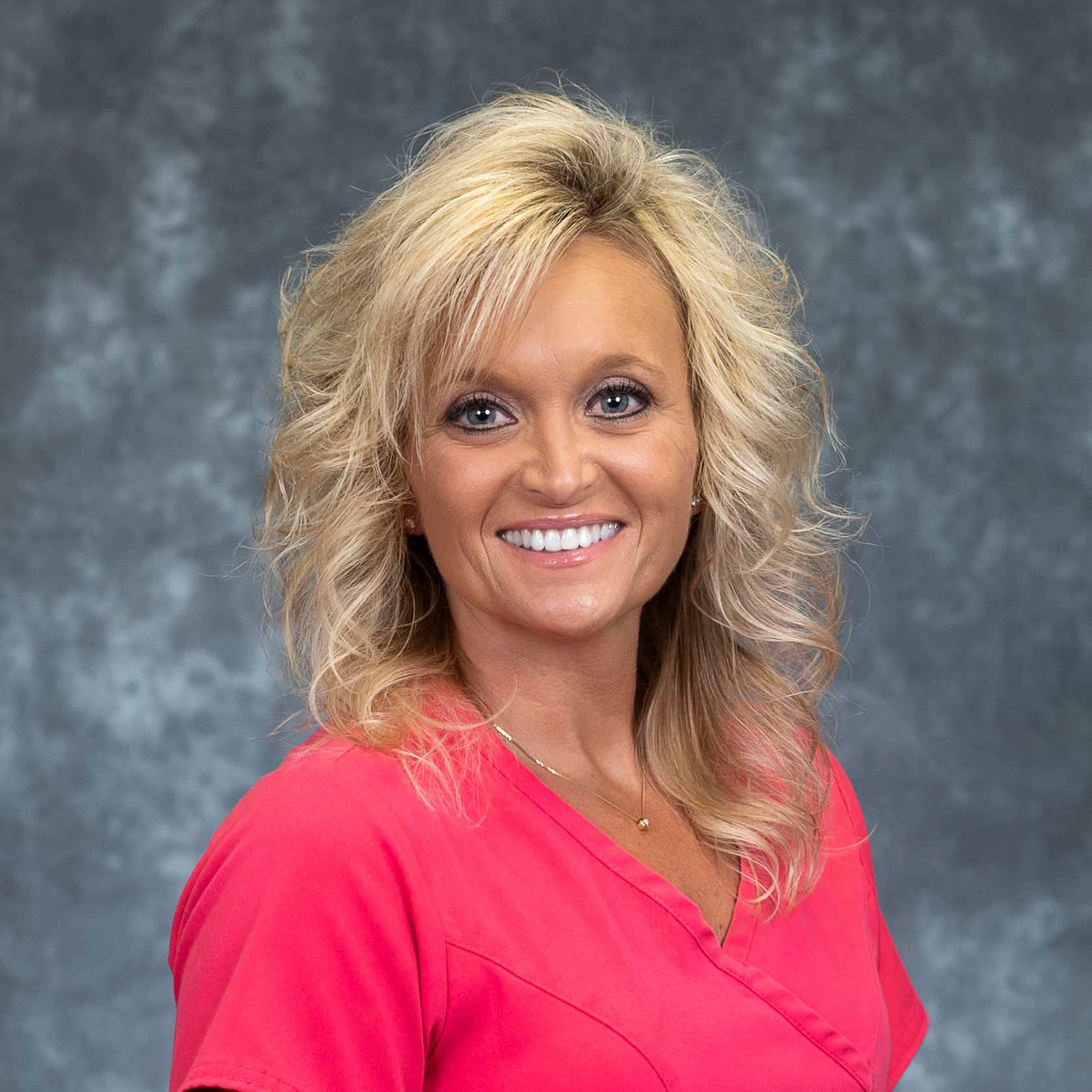 A woman in a pink scrub top is smiling for the camera.