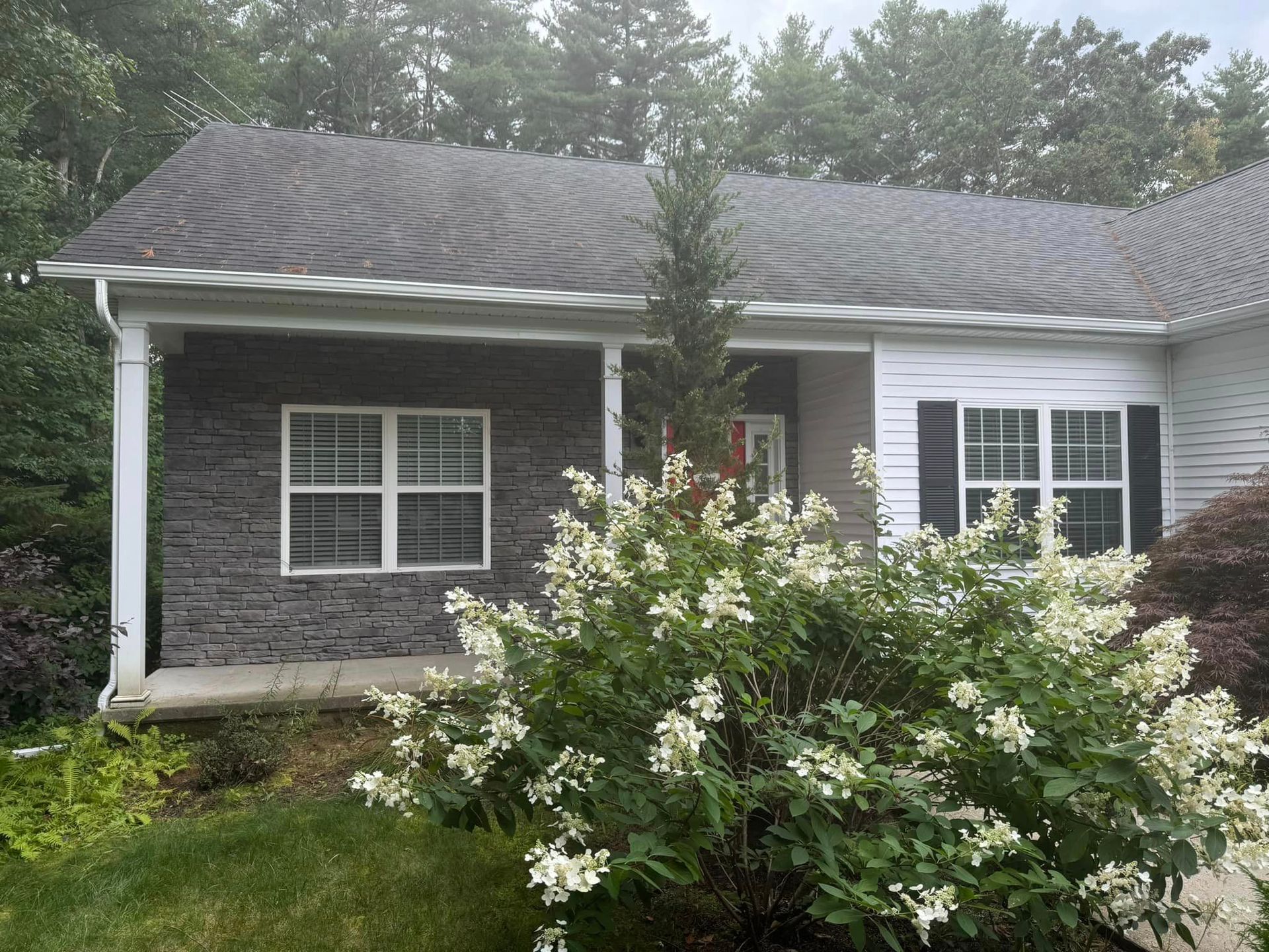 A small house with a porch and a bush in front of it