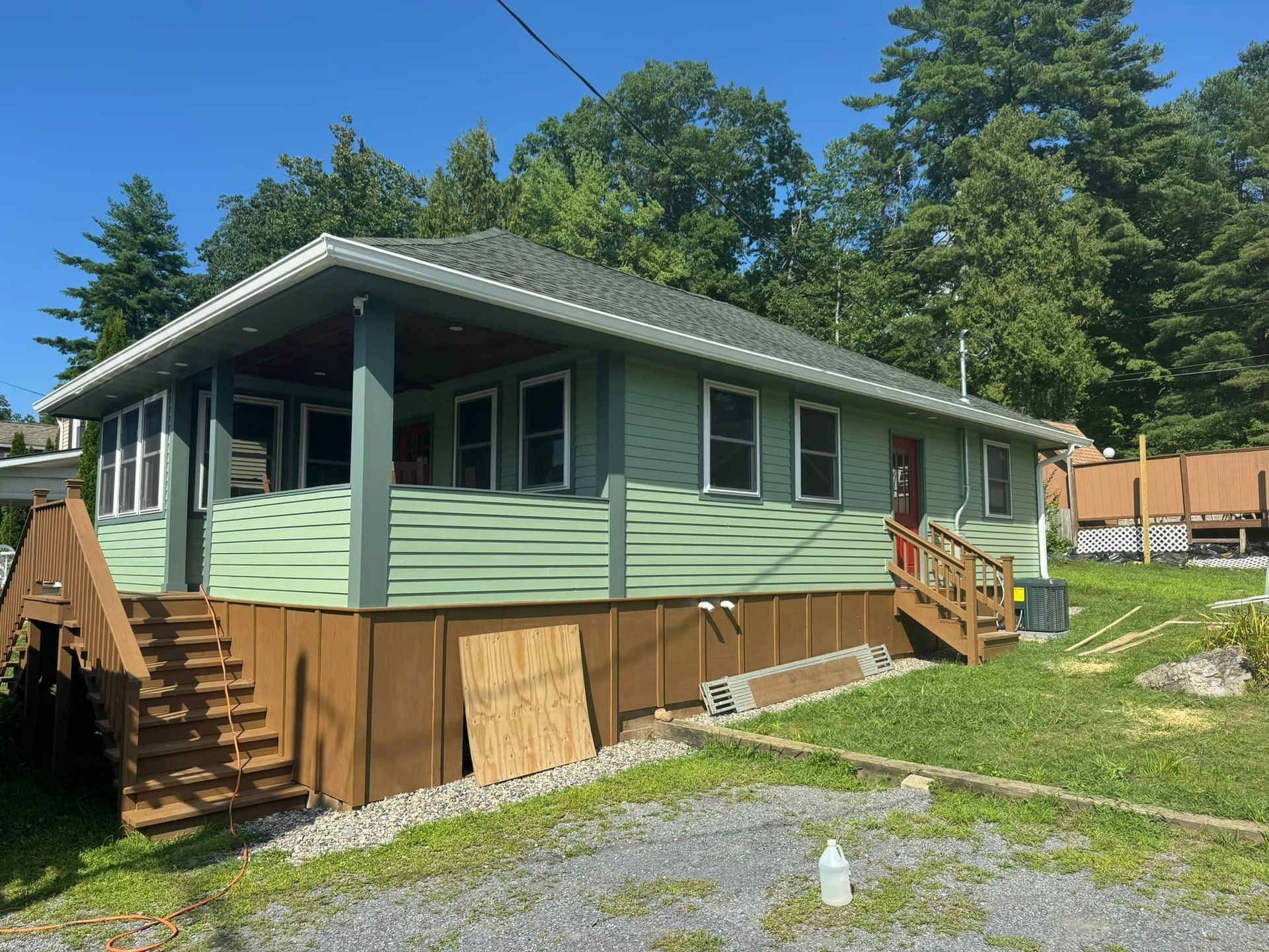 A green house with a porch and stairs is sitting on top of a grassy hill
