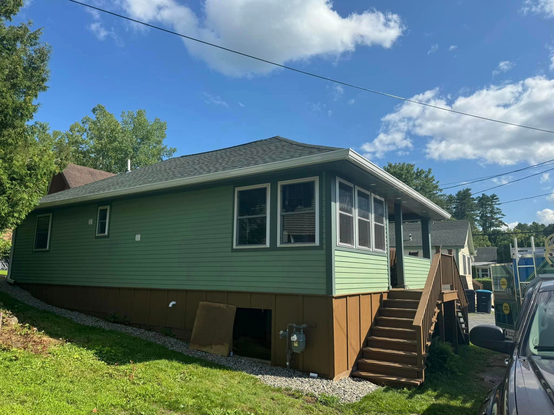A green house with stairs and a car parked in front of it