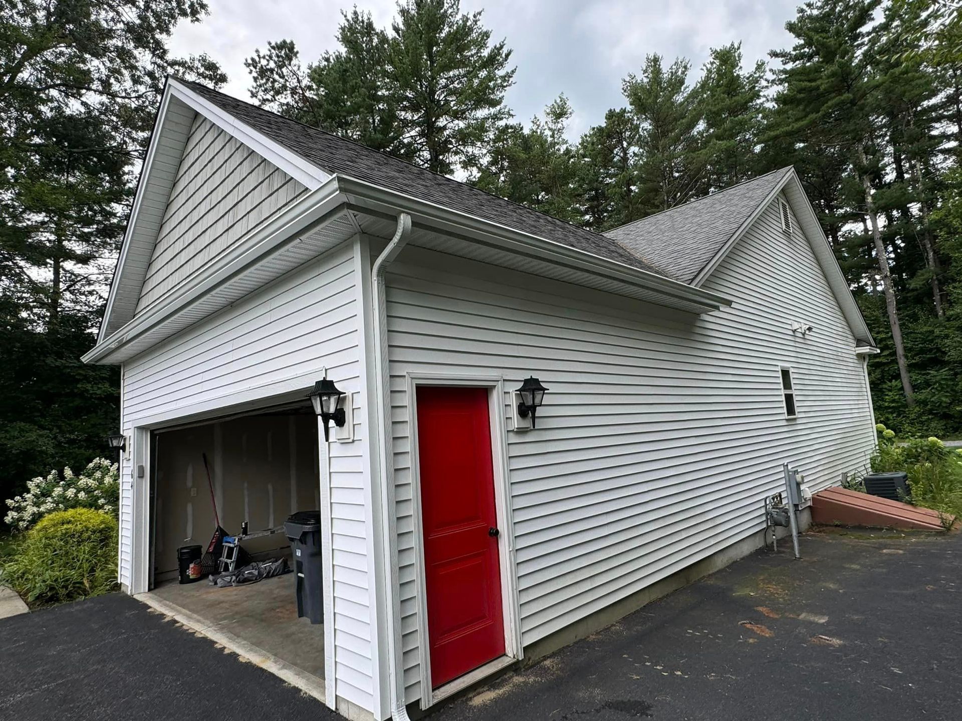 A white garage with a red door is surrounded by trees