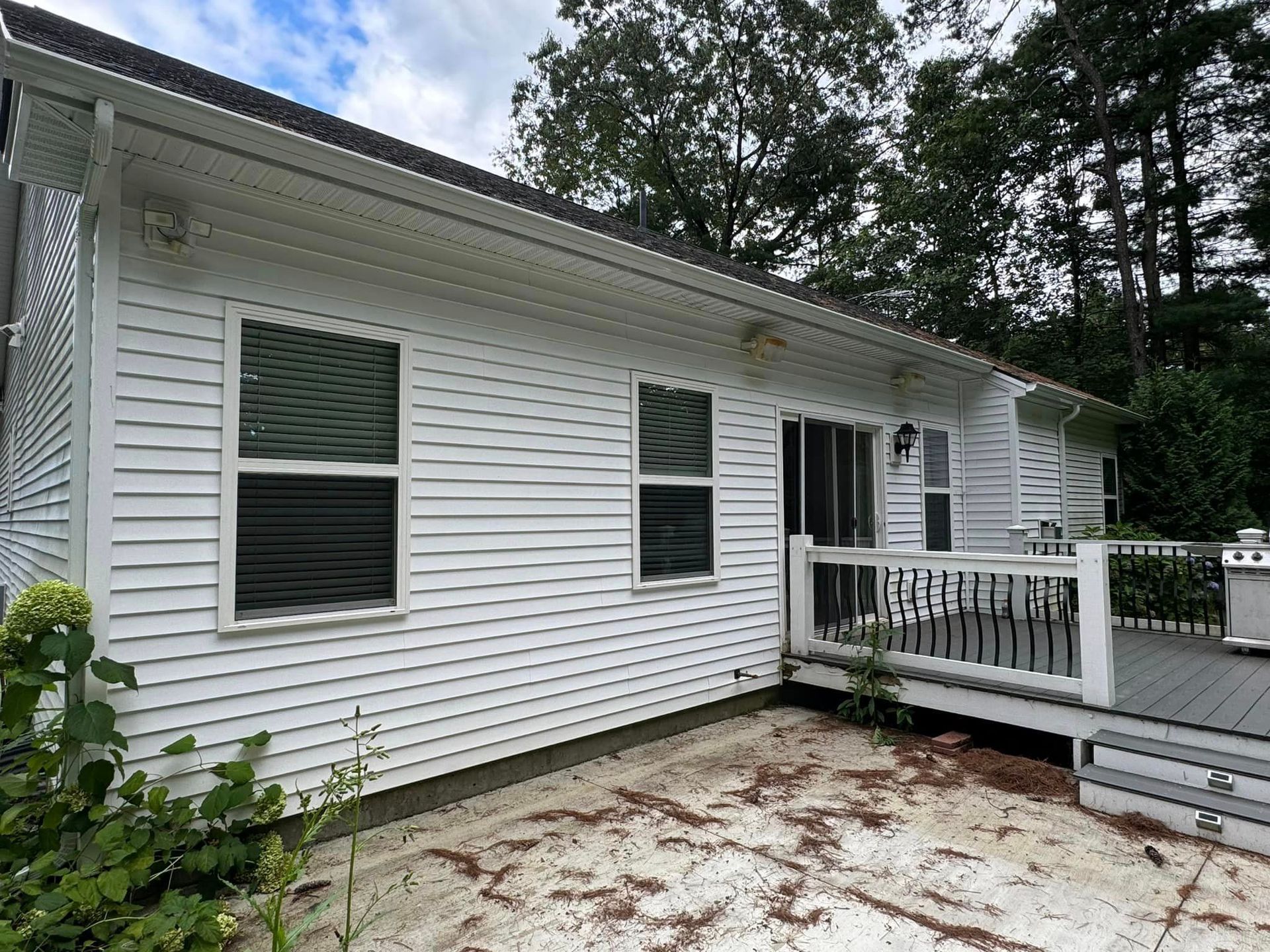 The back of a white house with a deck and trees in the background