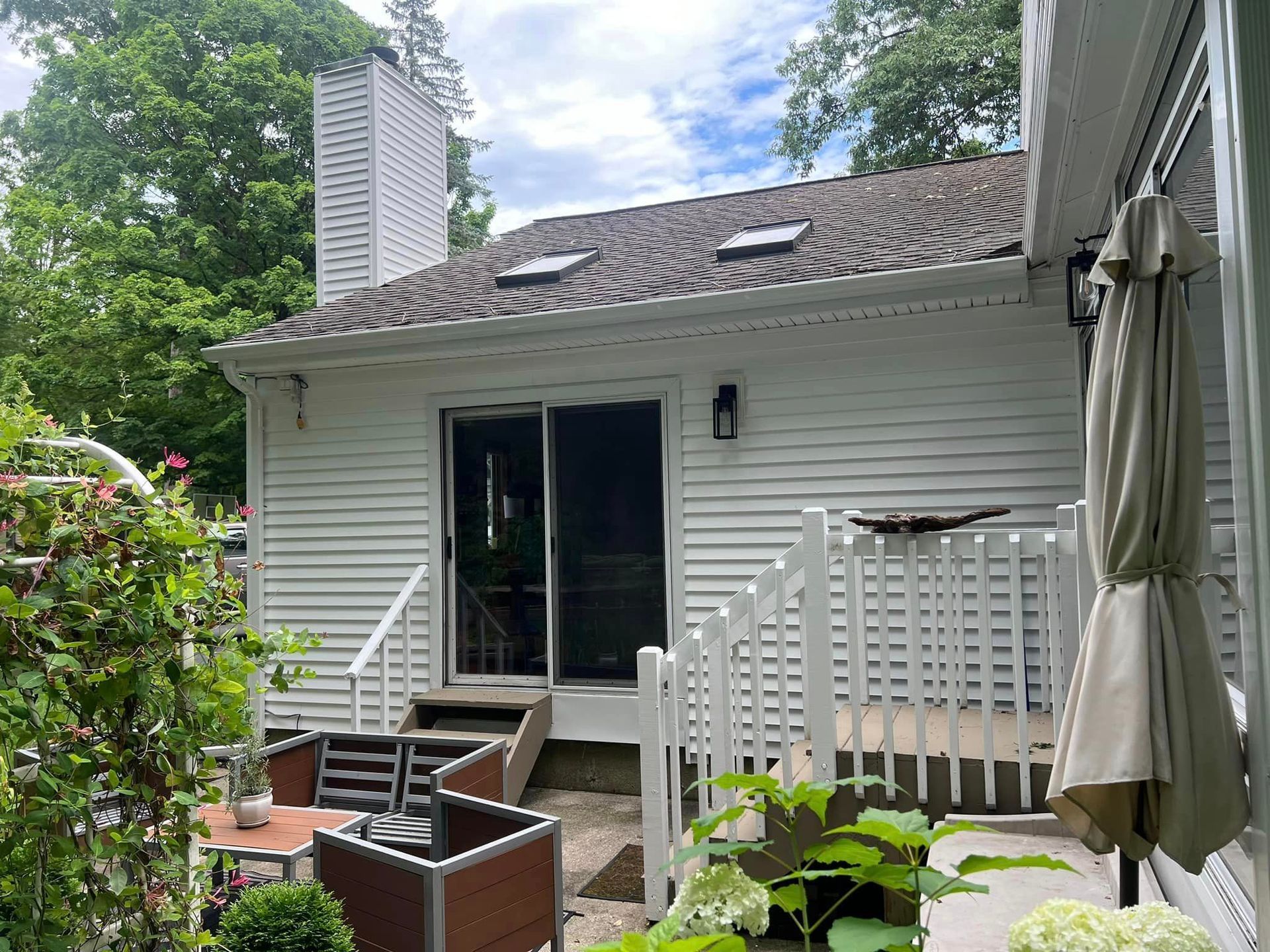 A white house with a sliding glass door and a deck with chairs and umbrellas