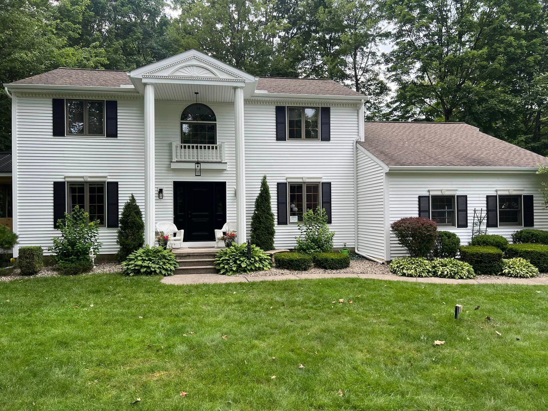 A large white house with black shutters and a large lawn in front of it