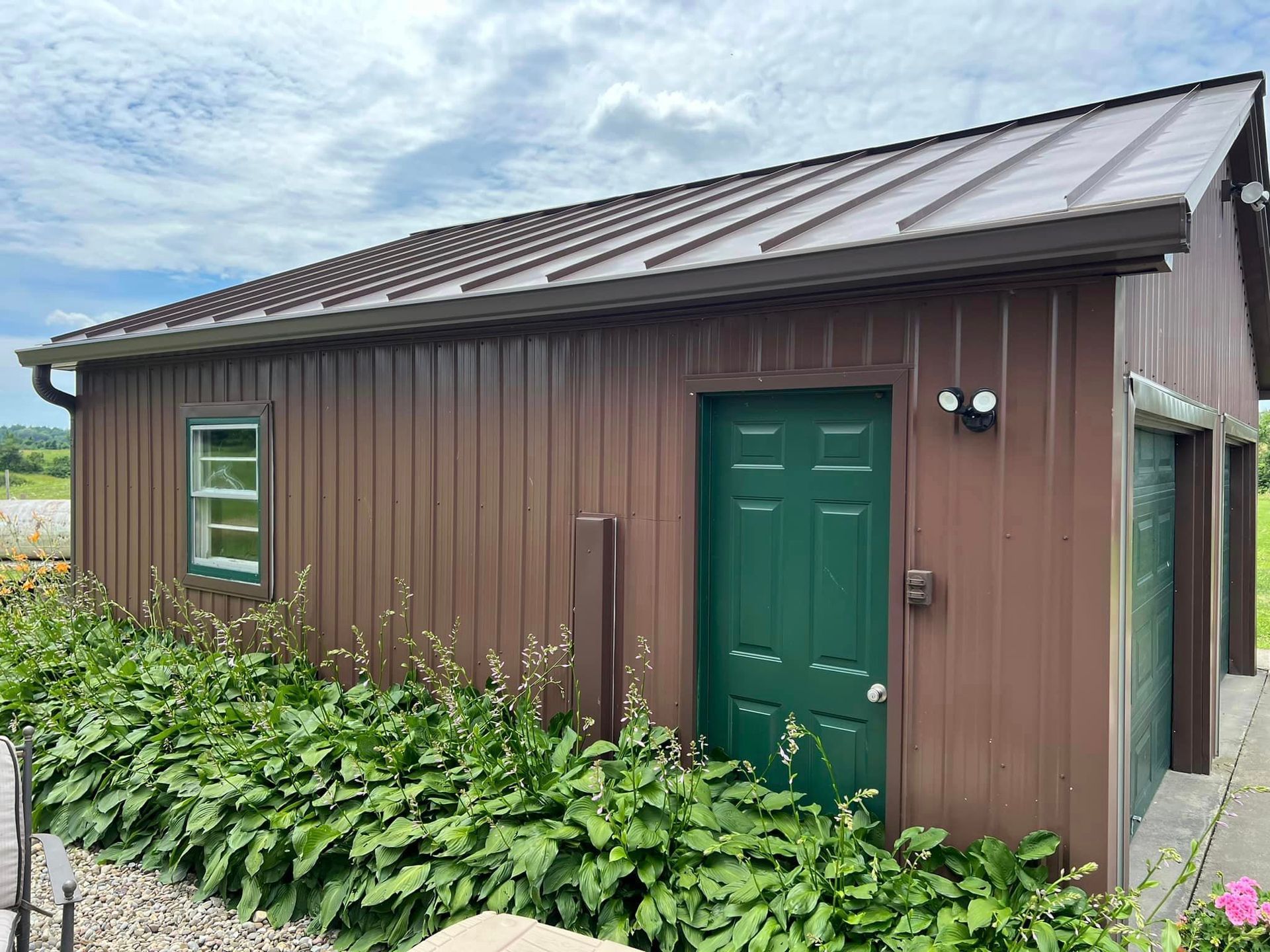 A brown building with a green door and window is surrounded by plants