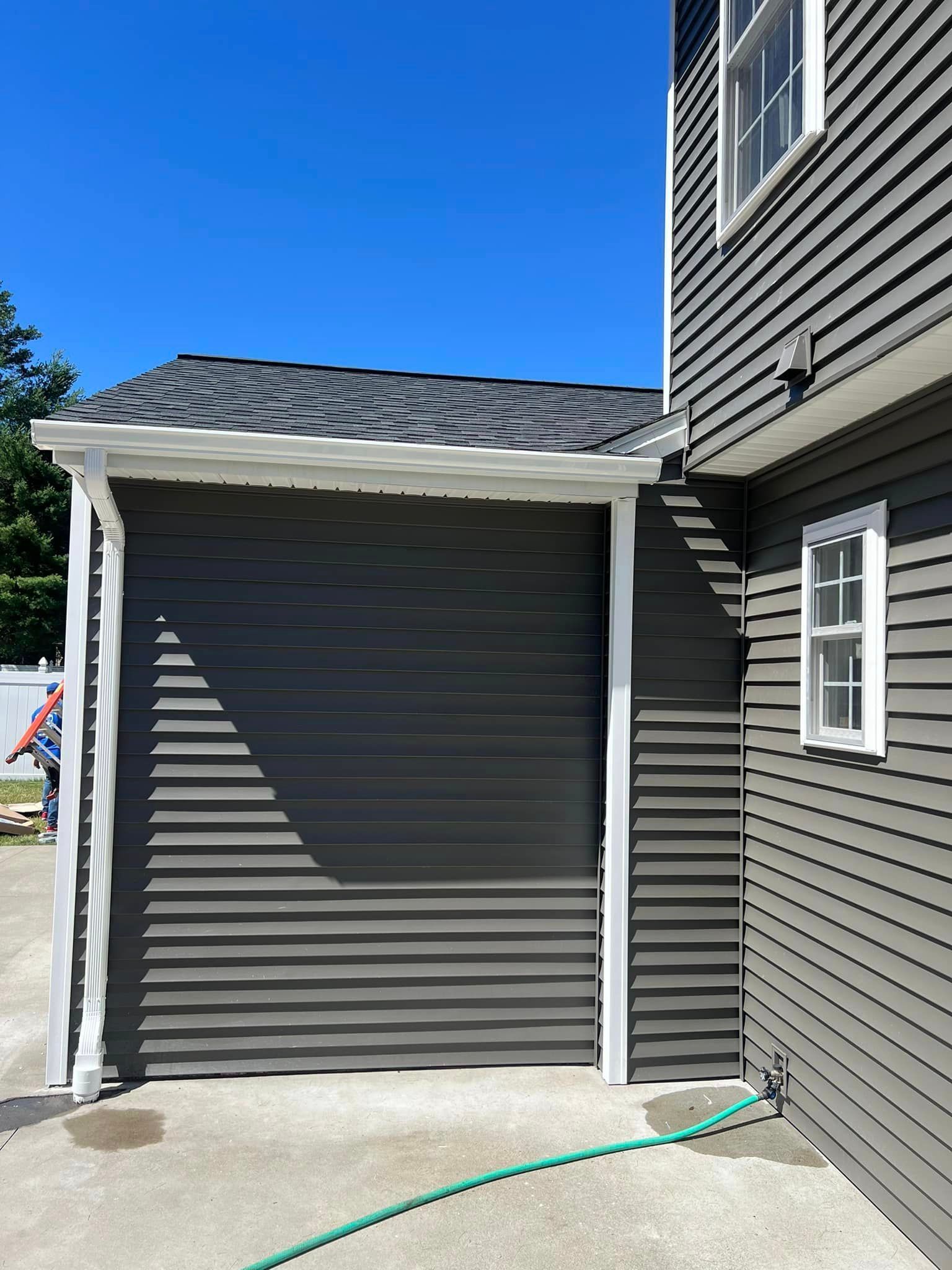 A house with a gray siding and a green hose next to it