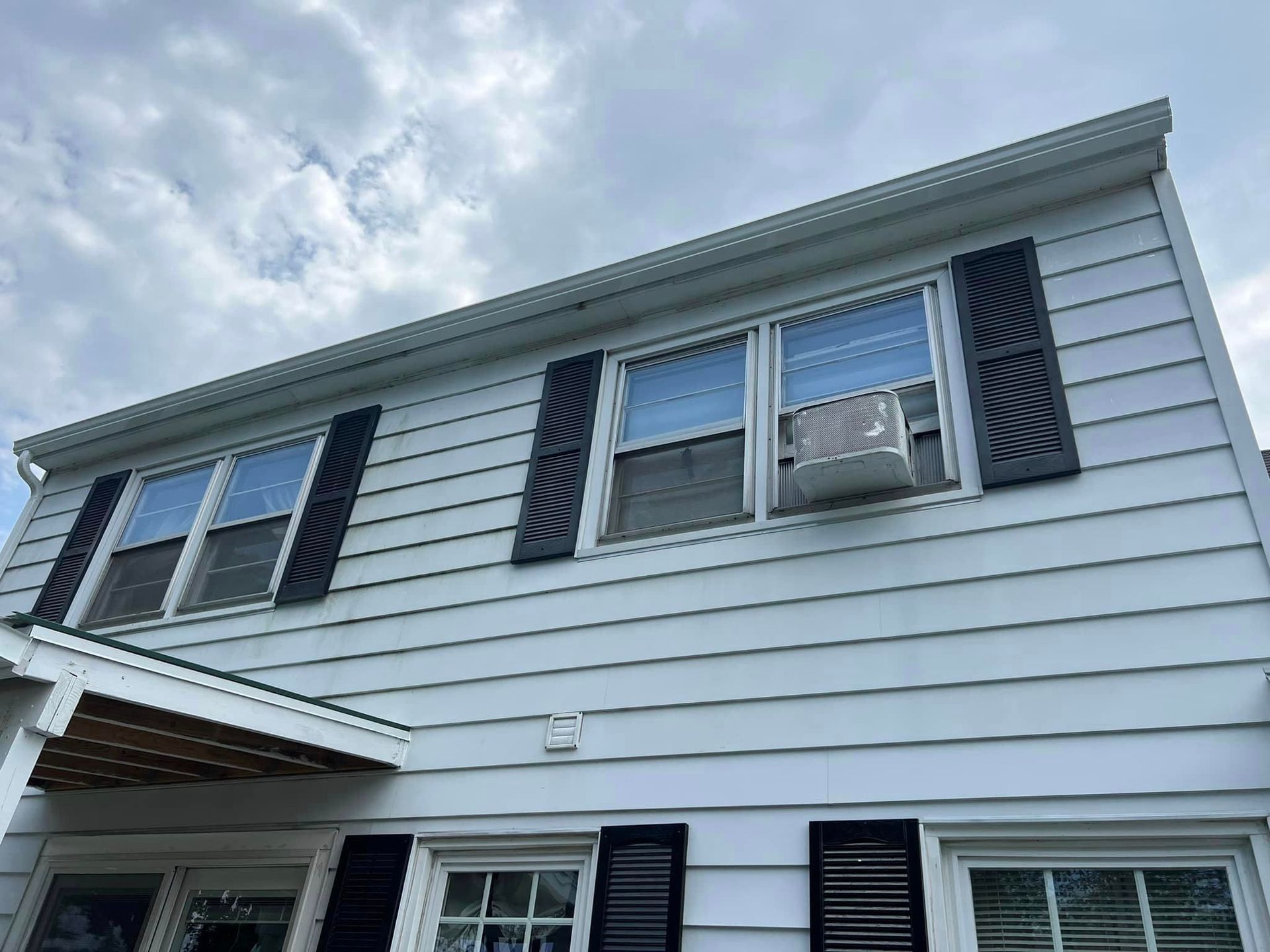A white house with black shutters and a window air conditioner