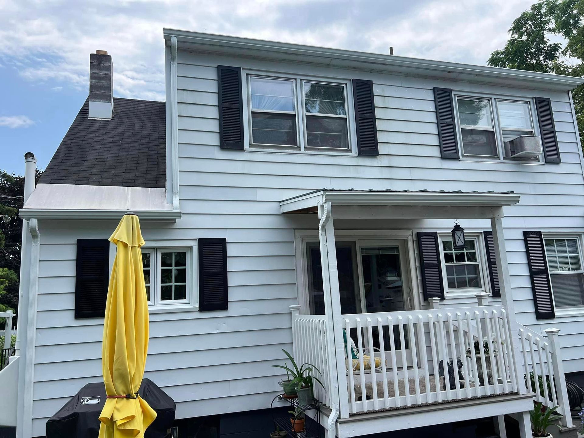 A white house with black shutters and a yellow umbrella on the porch