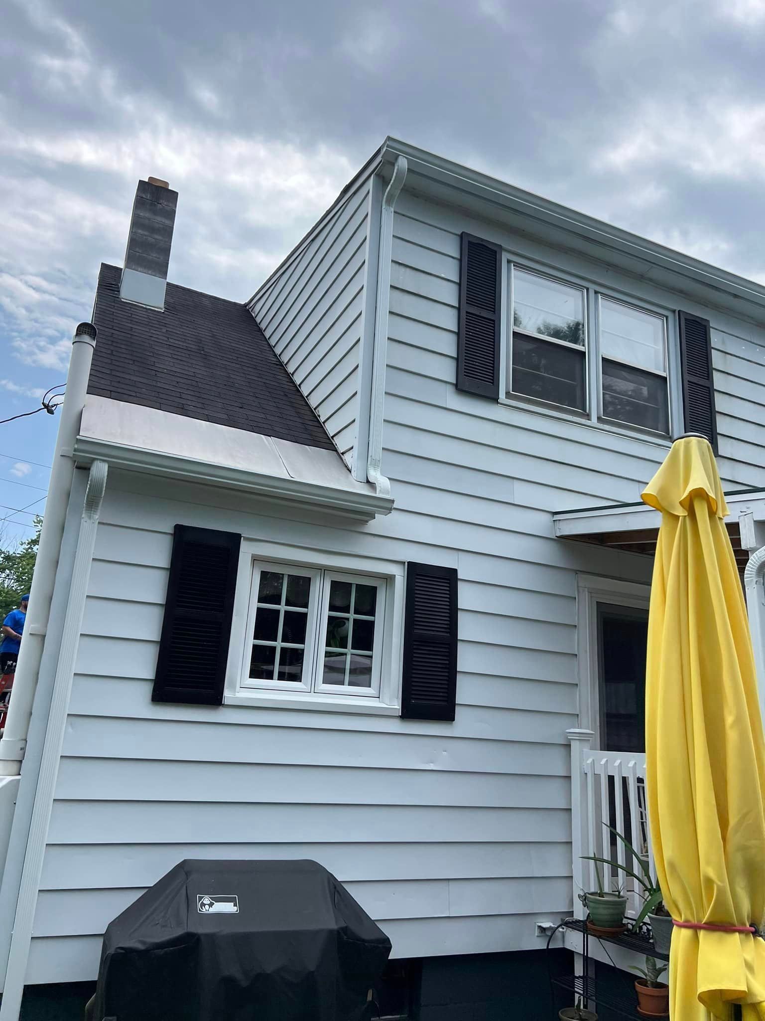 A white house with black shutters and a yellow umbrella in front of it
