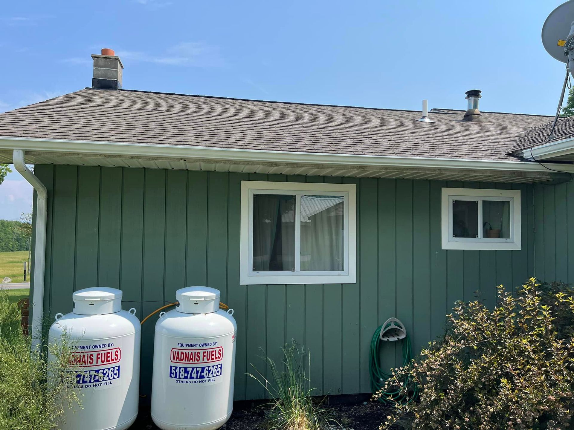 Two propane tanks are sitting on the side of a green house