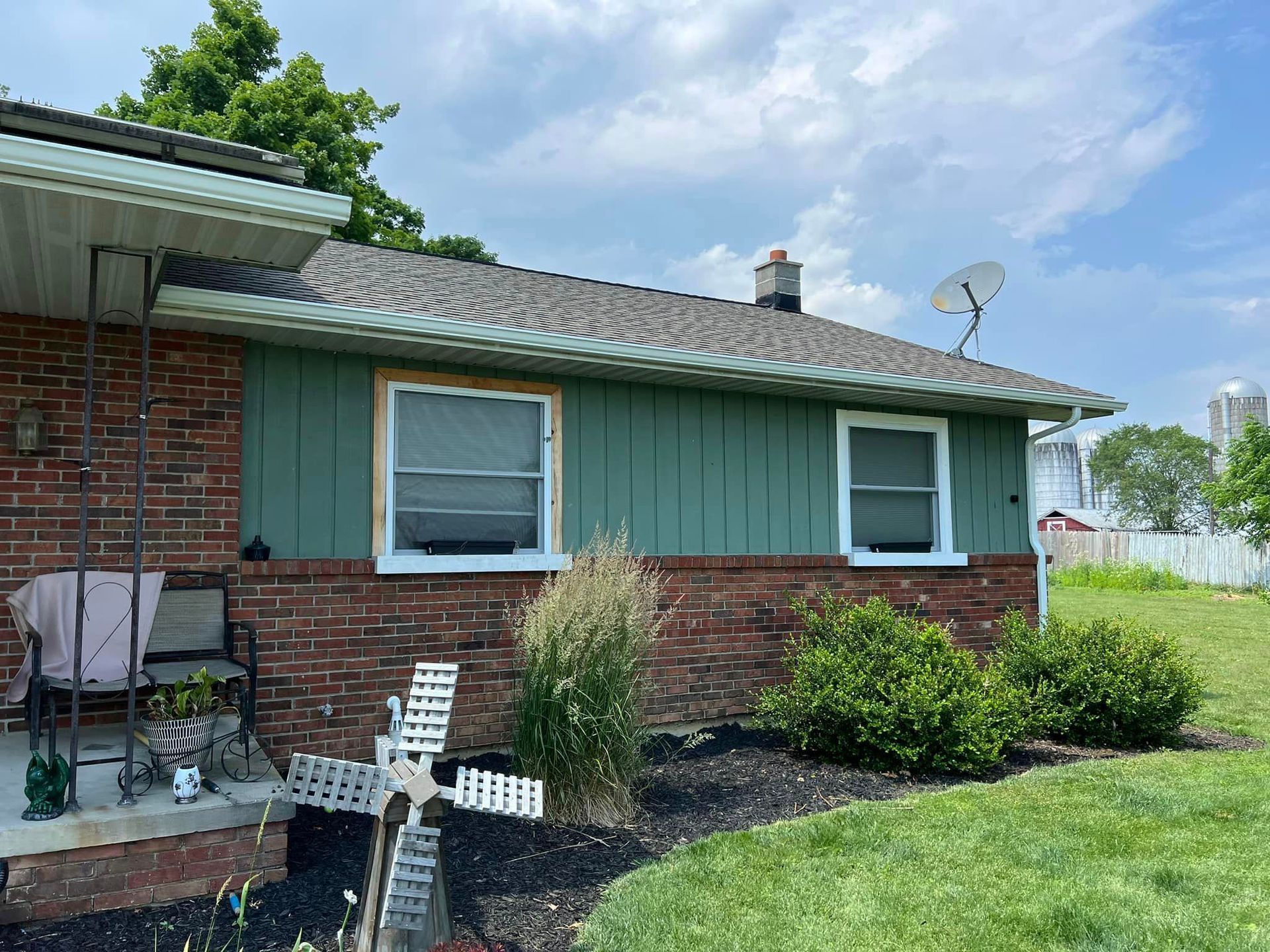 A brick house with a green siding and a windmill in front of it