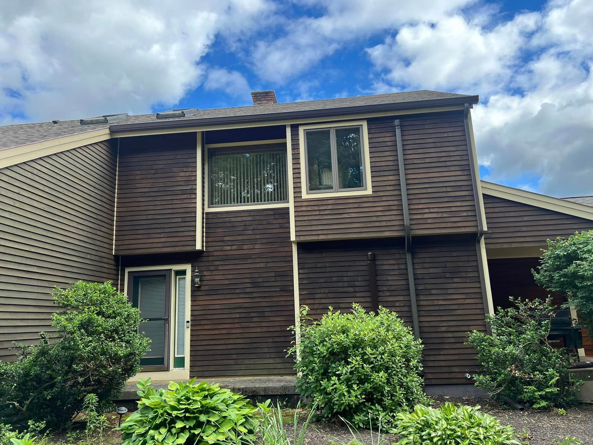 A large brown house with a lot of windows and bushes in front of it