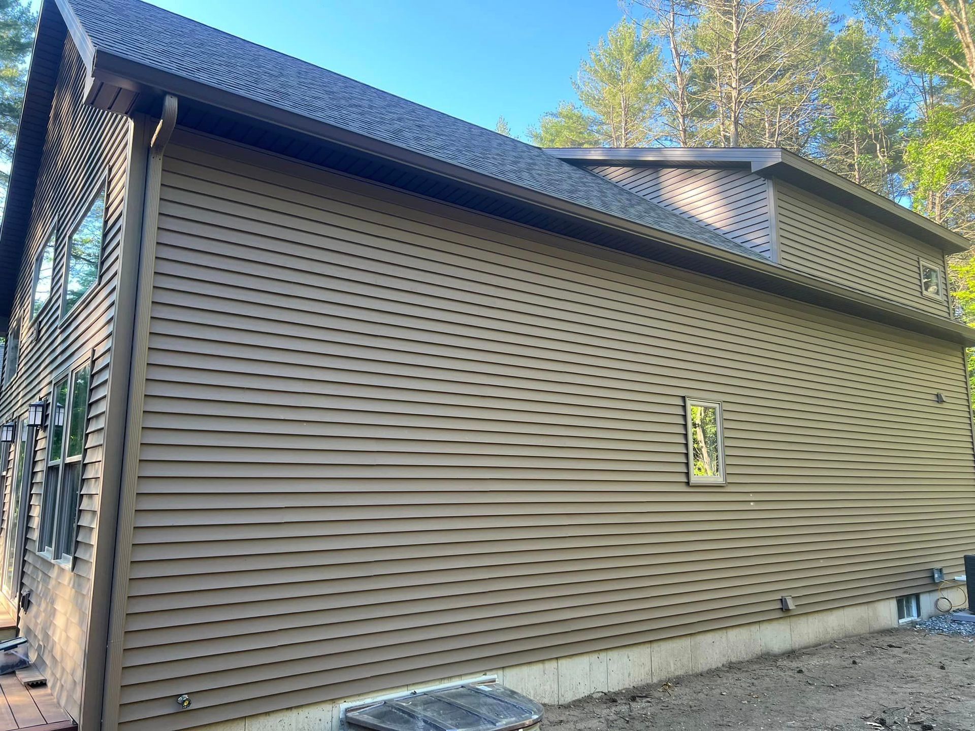 A large brown house with a black roof is sitting on top of a dirt field