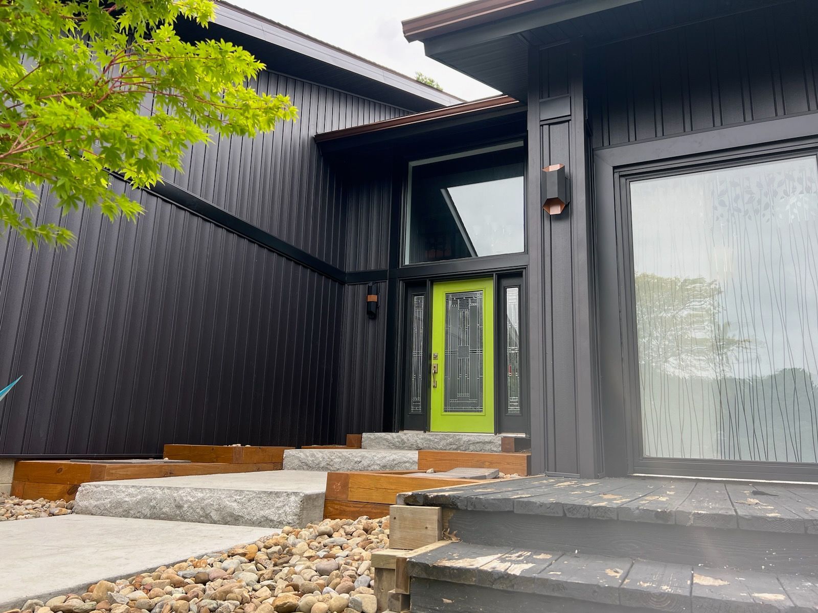 Black house with lime green door, stone steps, and light-colored windows.