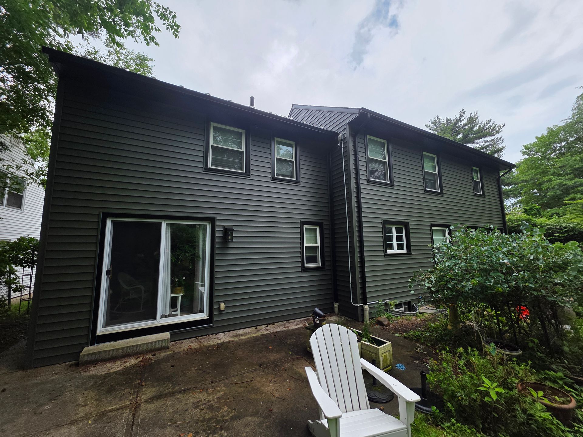 Dark gray house exterior with a sliding glass door and a white Adirondack chair on the patio.