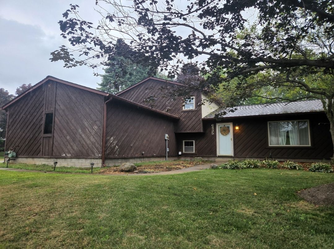 Brown house with white door, grass lawn, and overcast sky.
