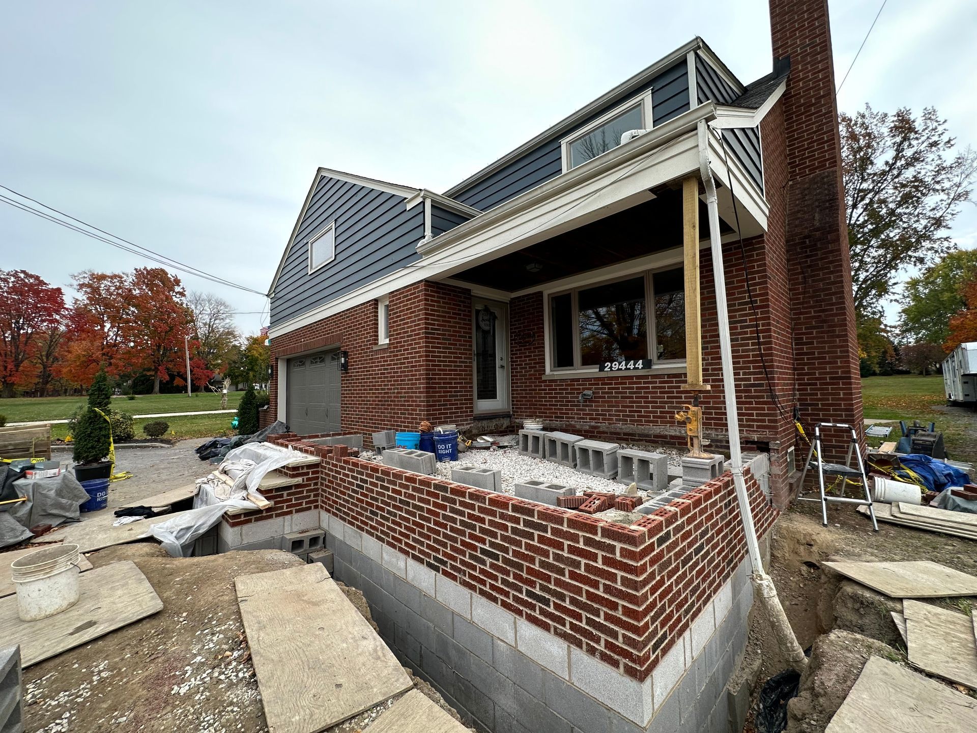 House under construction: brickwork on foundation, porch, blue siding, cloudy sky.