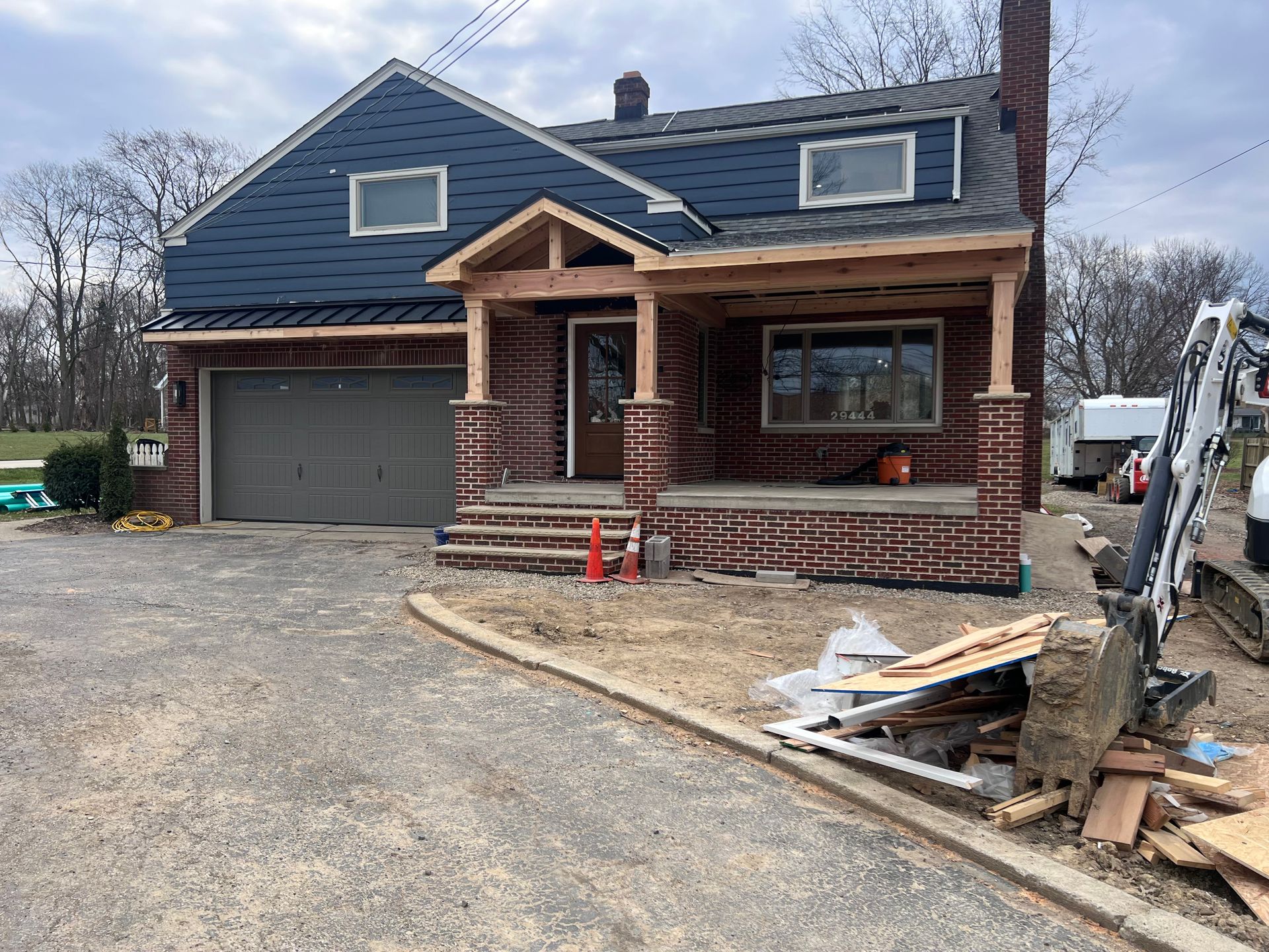 House under construction: red brick, blue siding, wooden porch, garage, and construction debris.