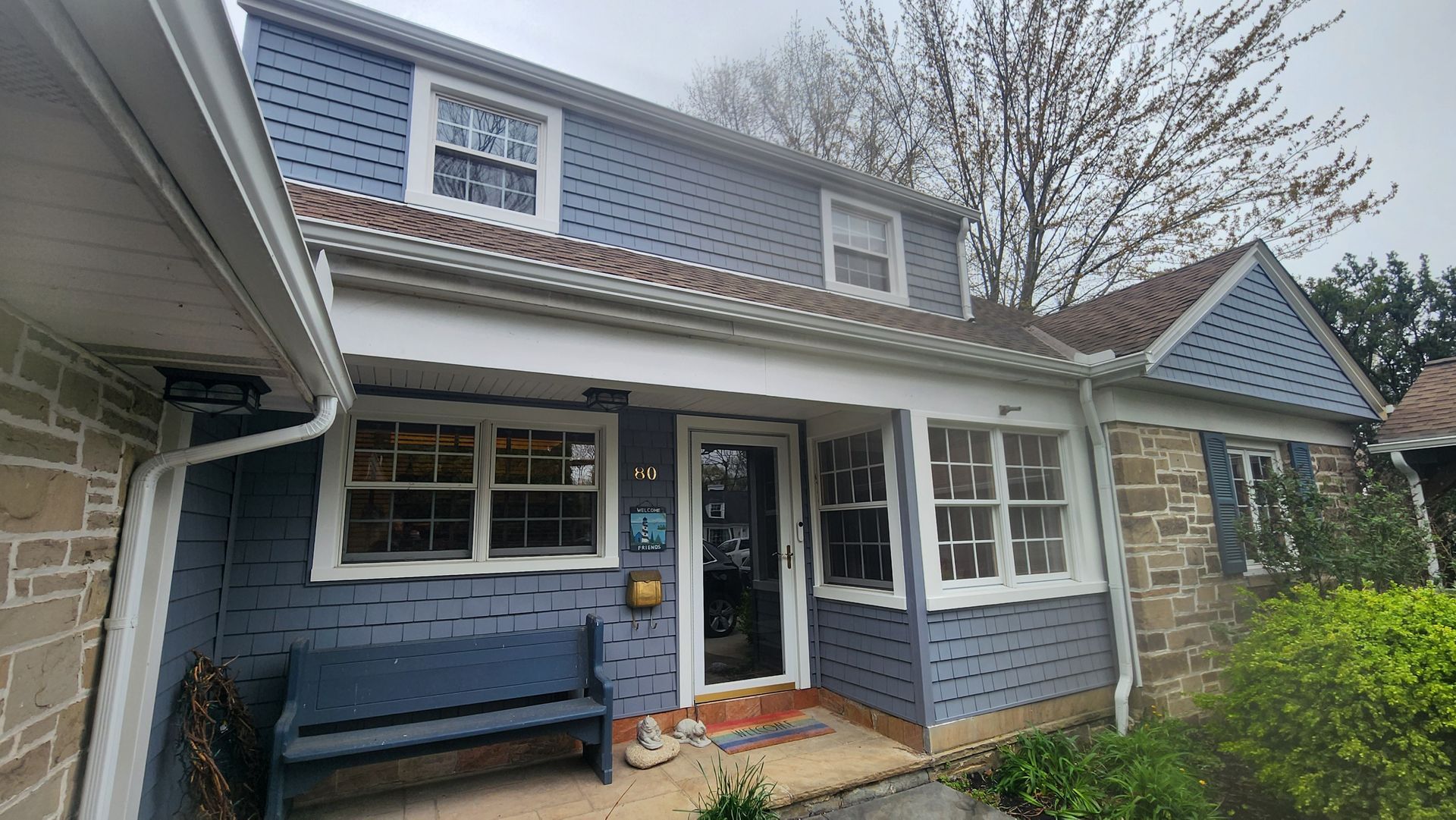 Blue-sided house with stone accents, a porch, and windows. A bench sits by the door.