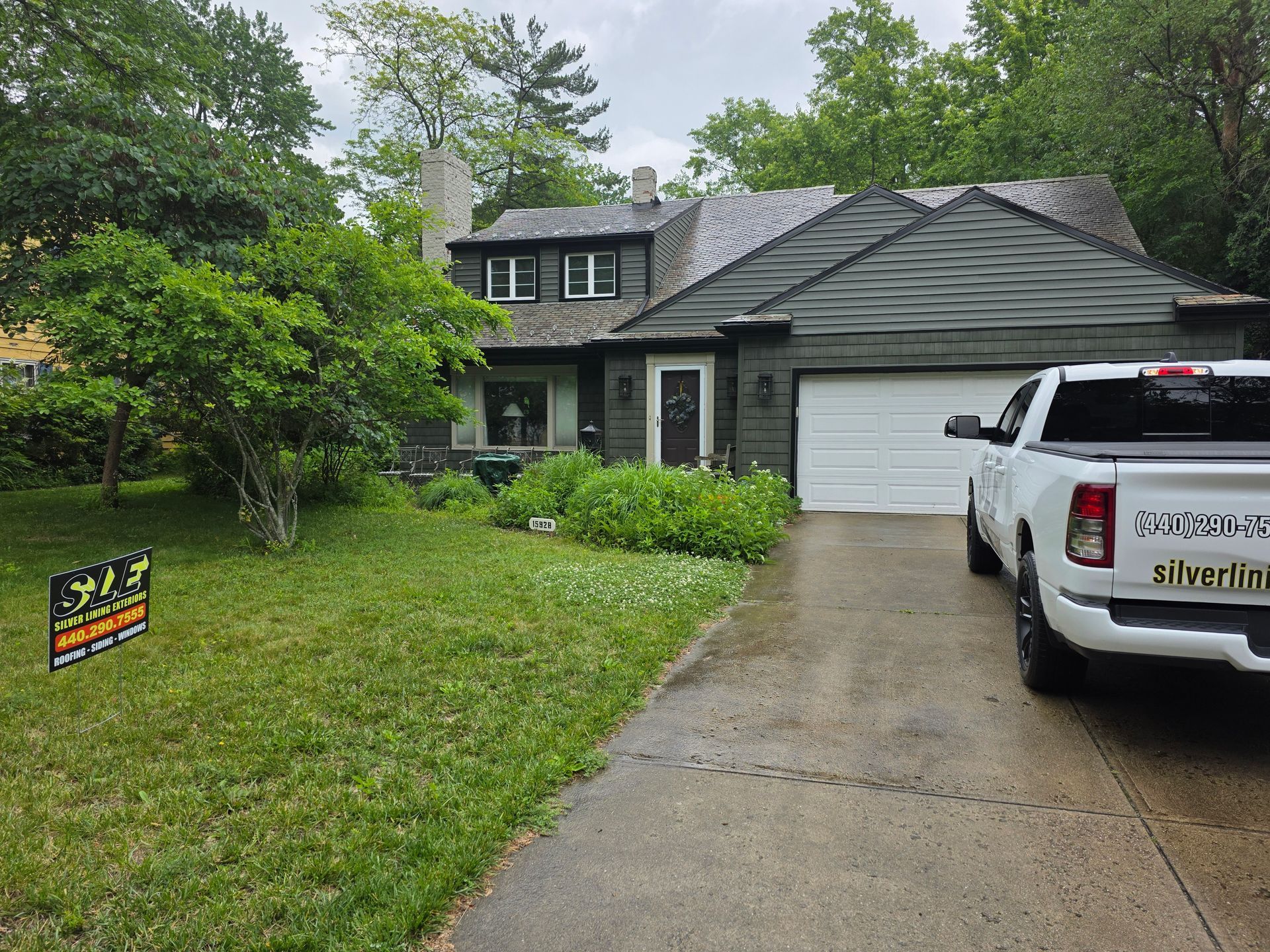 Green house with white garage door, parked truck, green lawn, sign.
