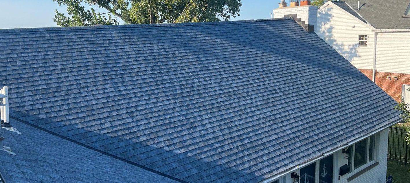 Blue asphalt shingle roof of a house, viewed from above on a sunny day.
