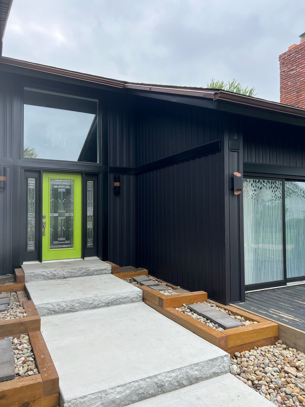 Black house with lime green door, concrete steps, and rock landscaping.