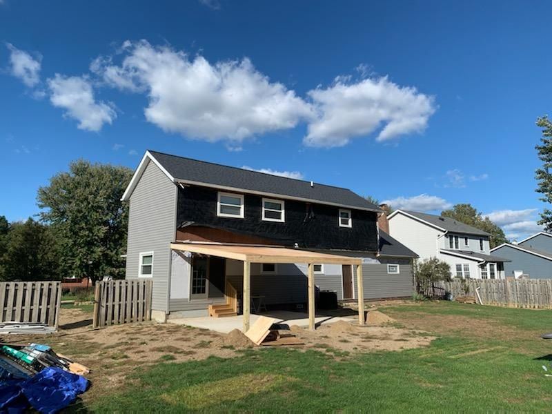 Back of a house under construction, with a partially built patio in a backyard, on a sunny day.