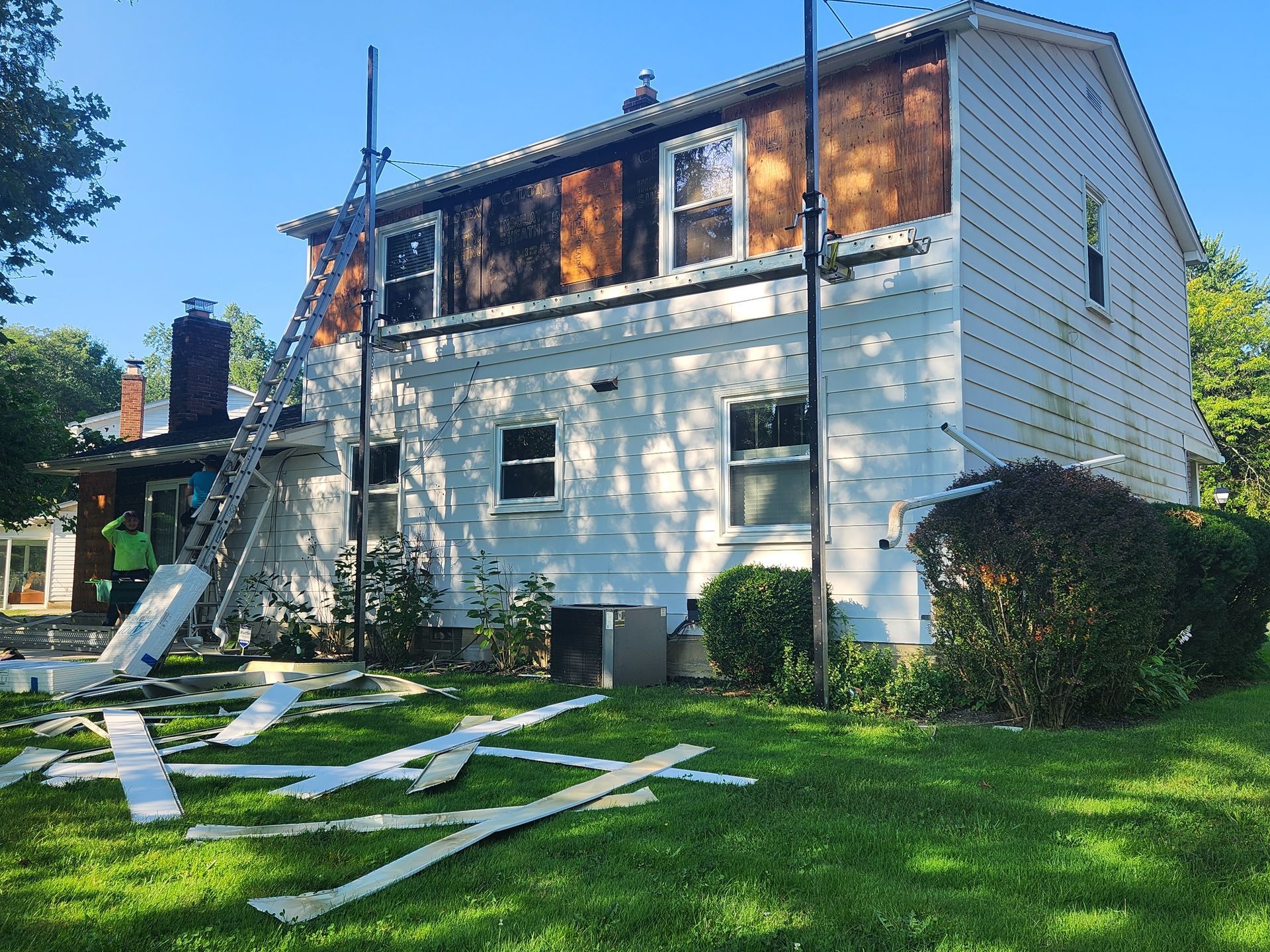 House exterior with fire damage to upper siding; workers near ladder, debris on lawn.