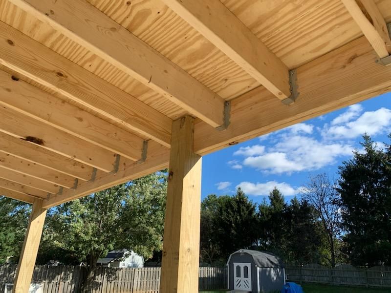 Wooden deck frame under construction. View of beams, sky, and backyard.