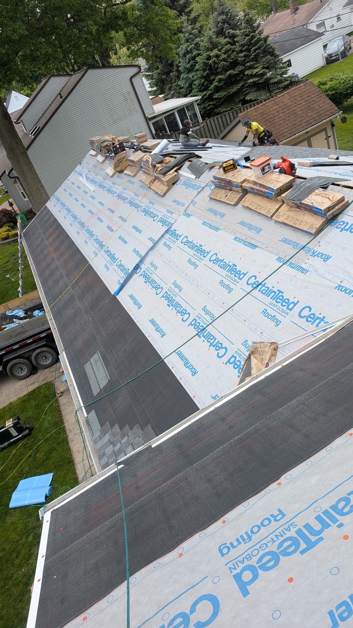 Roofers working on a house roof, partially covered with black shingles and blue underlayment.
