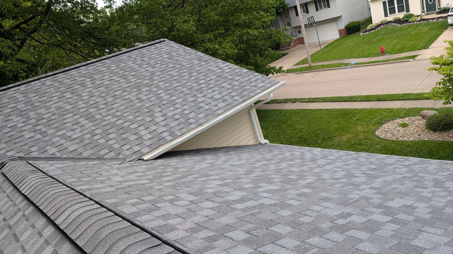 Gray asphalt shingle roof with white trim, overlooking a residential street with houses and green lawns.