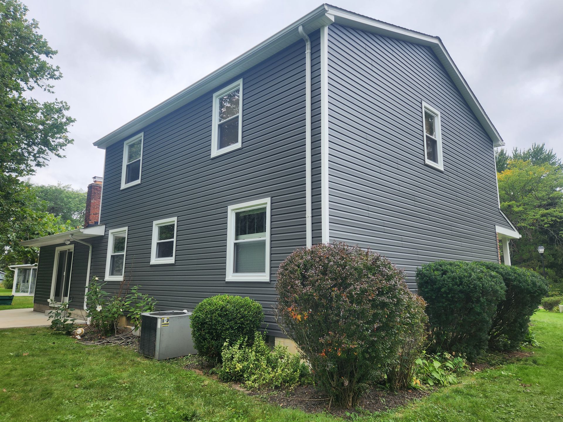 Dark gray house with white trim and windows, green yard, and cloudy sky.