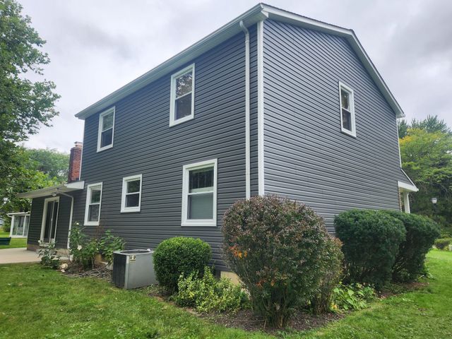 Dark gray house with white trim and windows, green yard, and cloudy sky.
