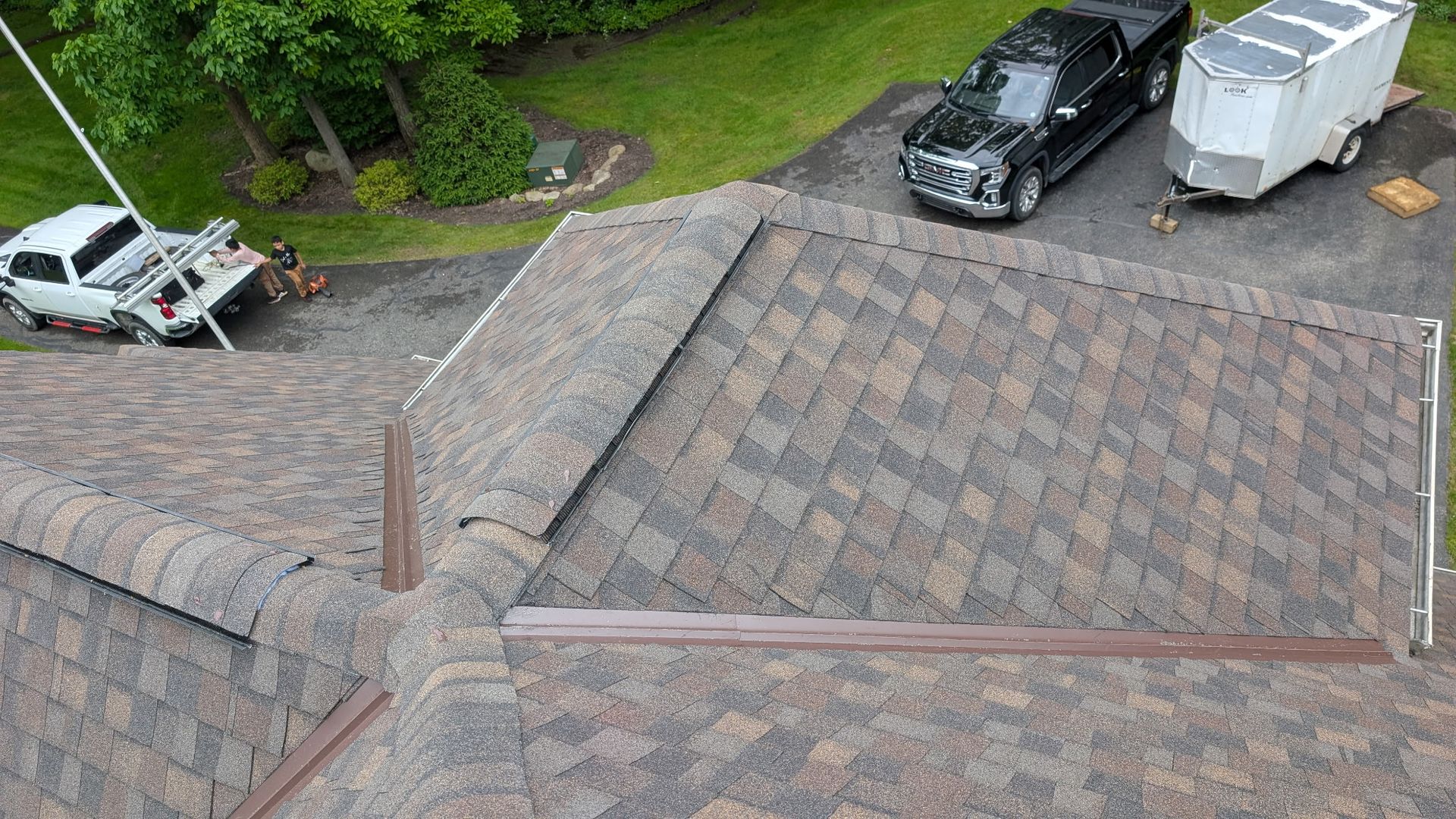 Overhead view of a multi-toned asphalt shingle roof with vehicles parked on a driveway.