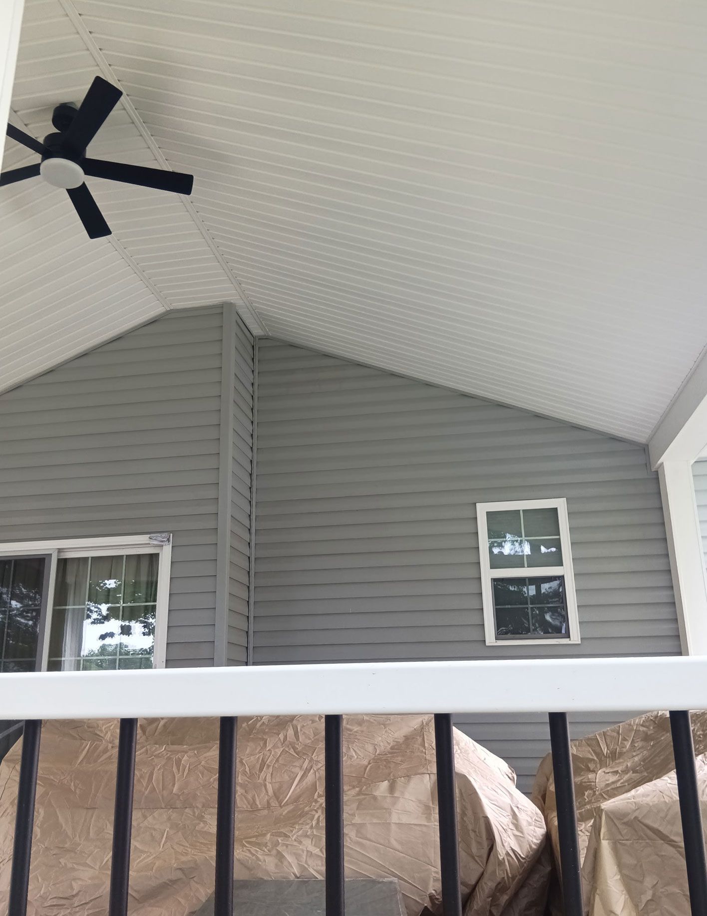 Gray siding on a house with a porch and ceiling fan; white trim, and a window visible.