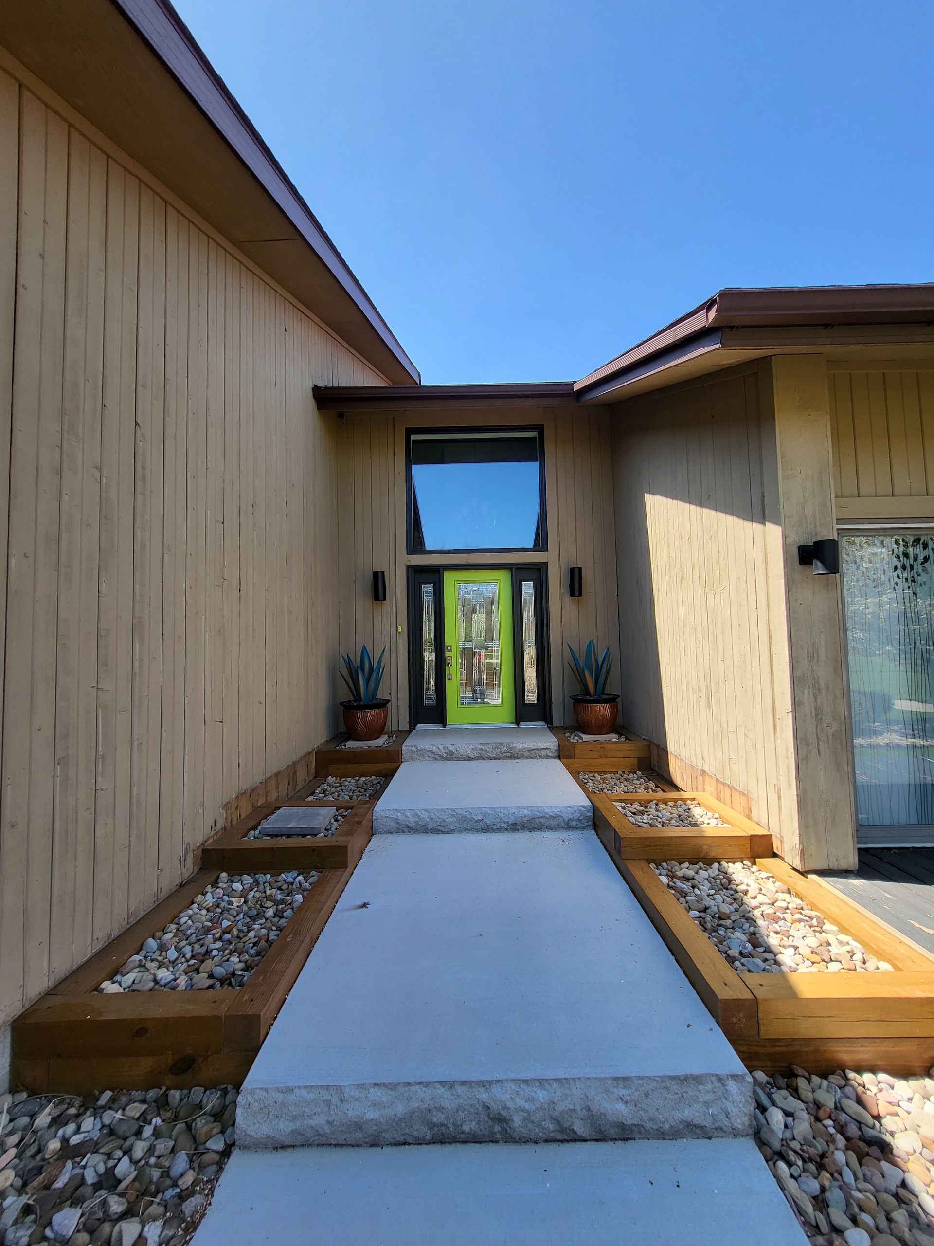 Entryway with a bright green door, cement path, wooden planters, and beige siding.