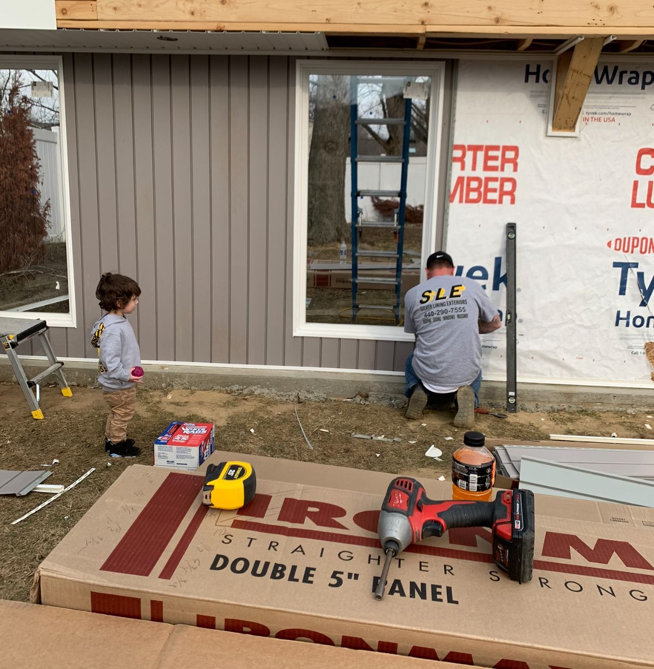 A man and a child watch a construction project. The man is working on a window.
