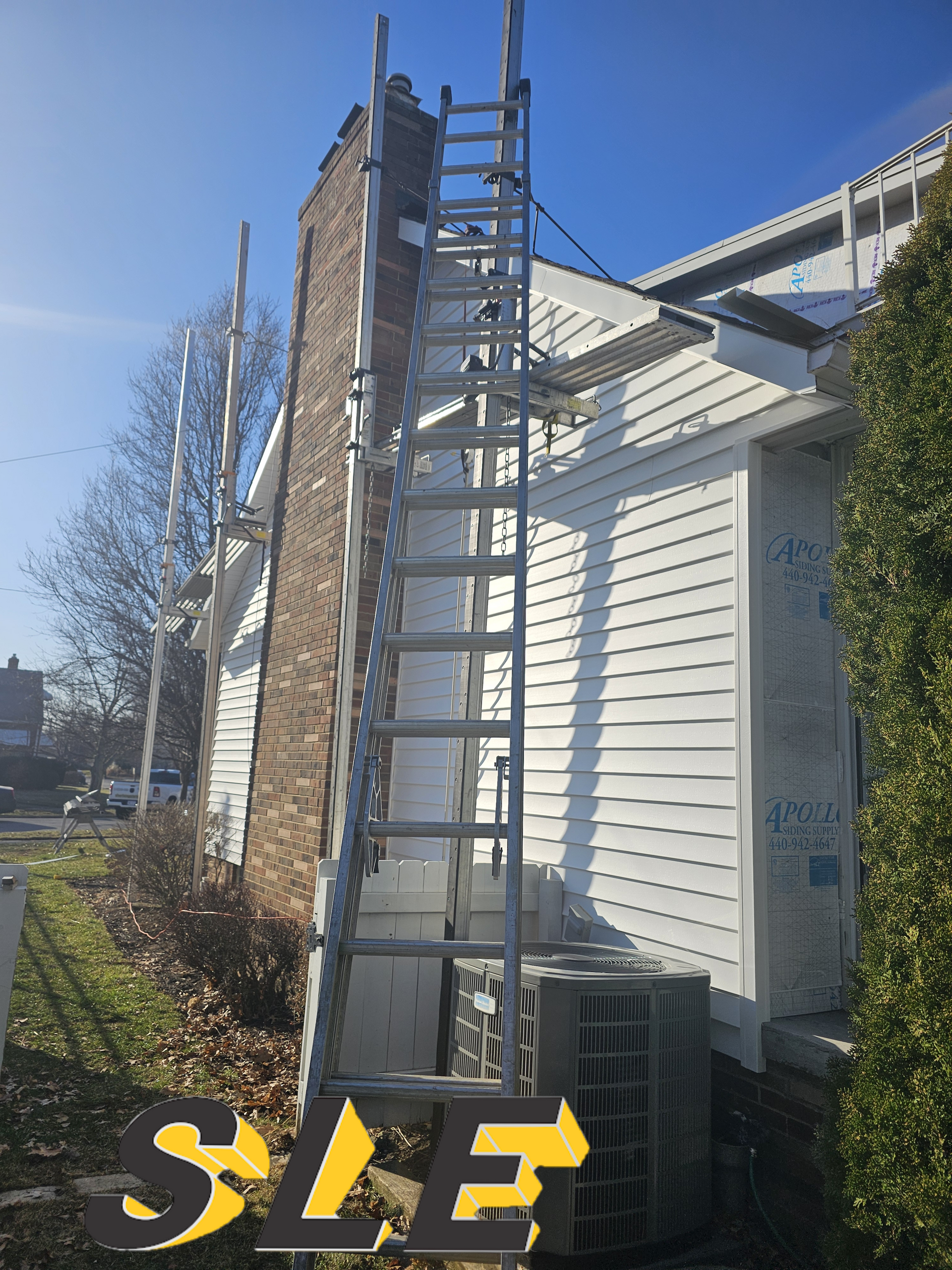 Ladder leaned against a brick chimney on a white house; an air conditioning unit is below the ladder.