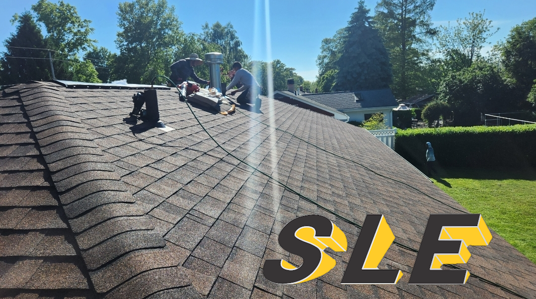 Roofers on a brown shingle roof with a blue sky background. SLE logo in lower right.