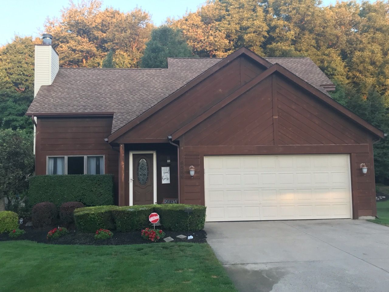 Brown house with beige garage door, brown roof, and manicured front lawn.