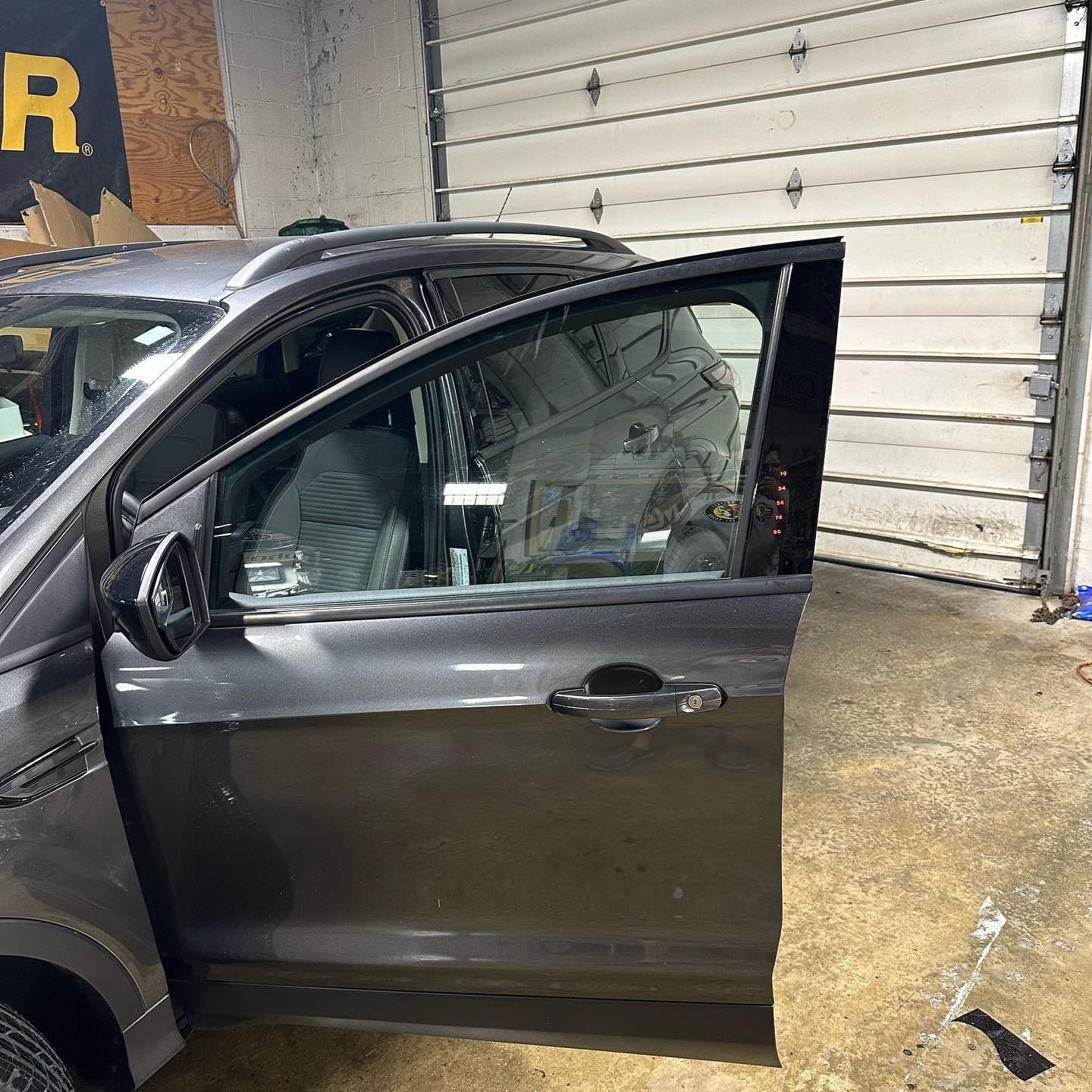 Dark SUV with driver door open in a garage, showing a shattered side window.