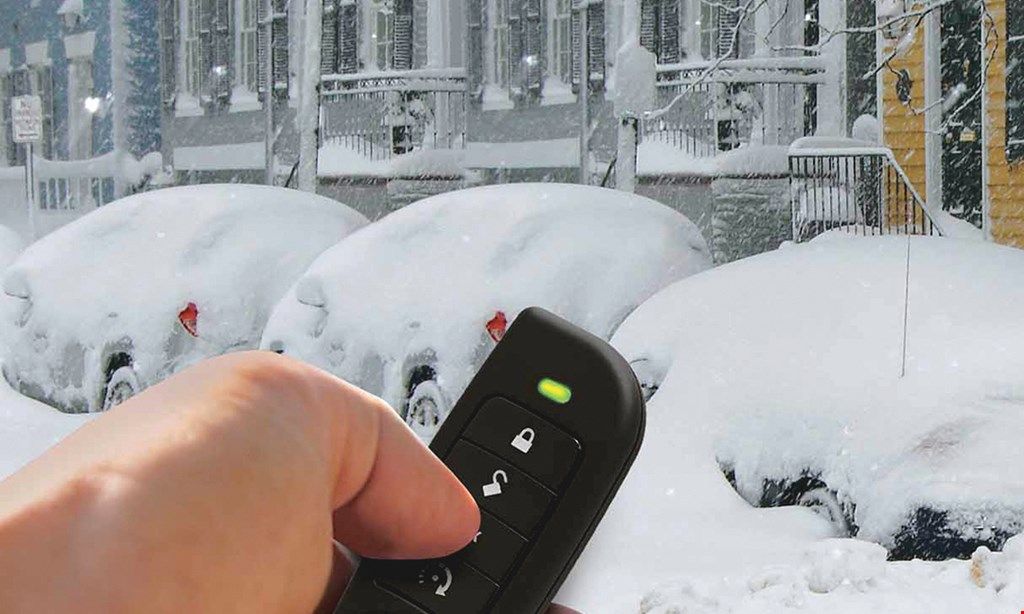 Hand holding a car key fob pointed at snow-covered cars in a snowy parking lot