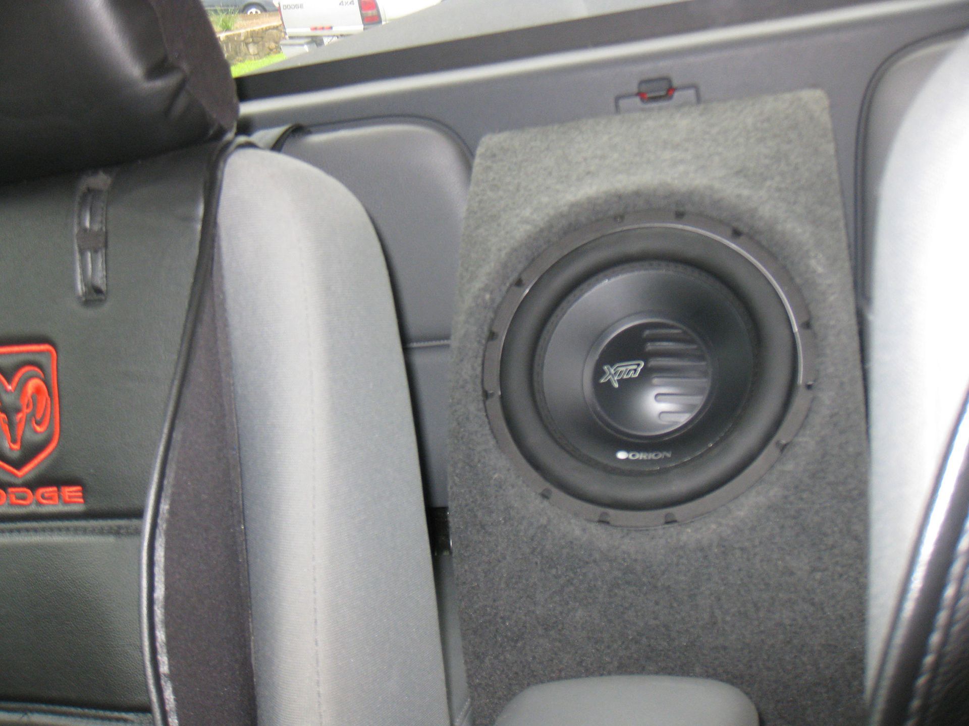 Car trunk with a black subwoofer mounted in a gray speaker box beside seats